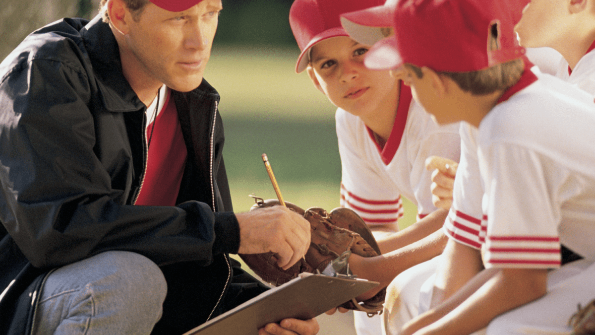 A male coach talking with his baseball players.