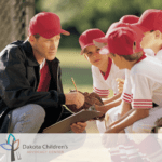 A male coach talking with his baseball players.