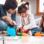 A woman (either a mother or caregiver) playing with a girl with building blocks.